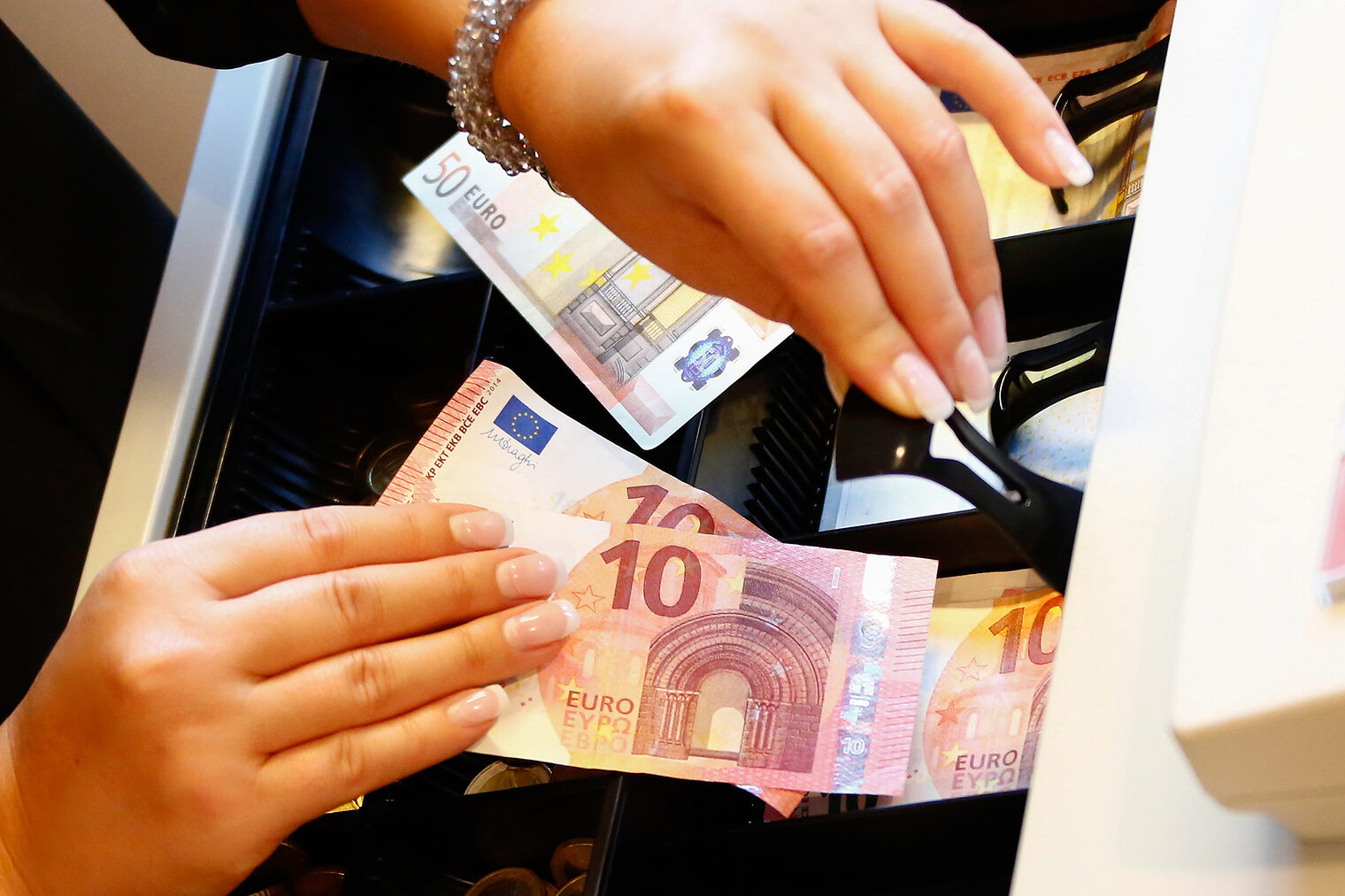 | Kasse | Bonpflicht | TSE | Kassen-Meldepflicht | Datensicherheit Nahaufnahme zweier Hände die Geld in eine Kasse einsortieren