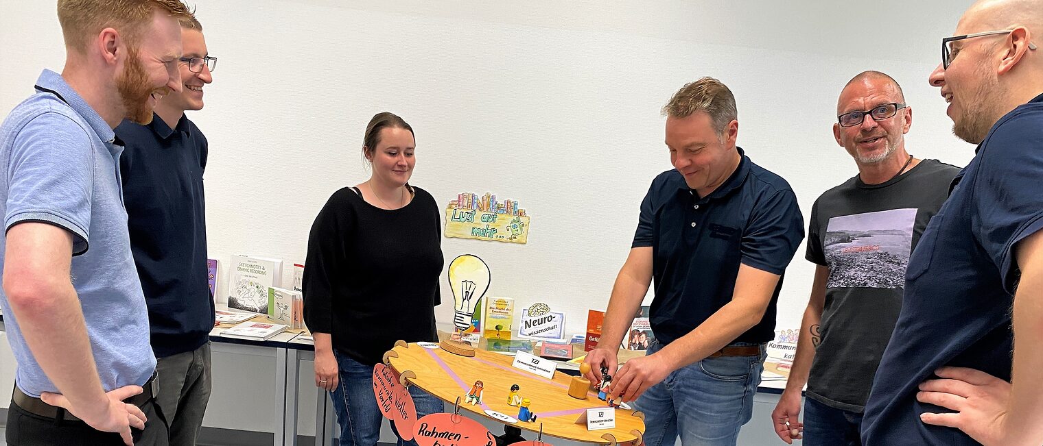 Kursteilnehmende von Train the Trainer Die Kursteilnehmenden von Train the Trainer stehen um einen runden Tisch und tauschen sich über ein Thema aus.