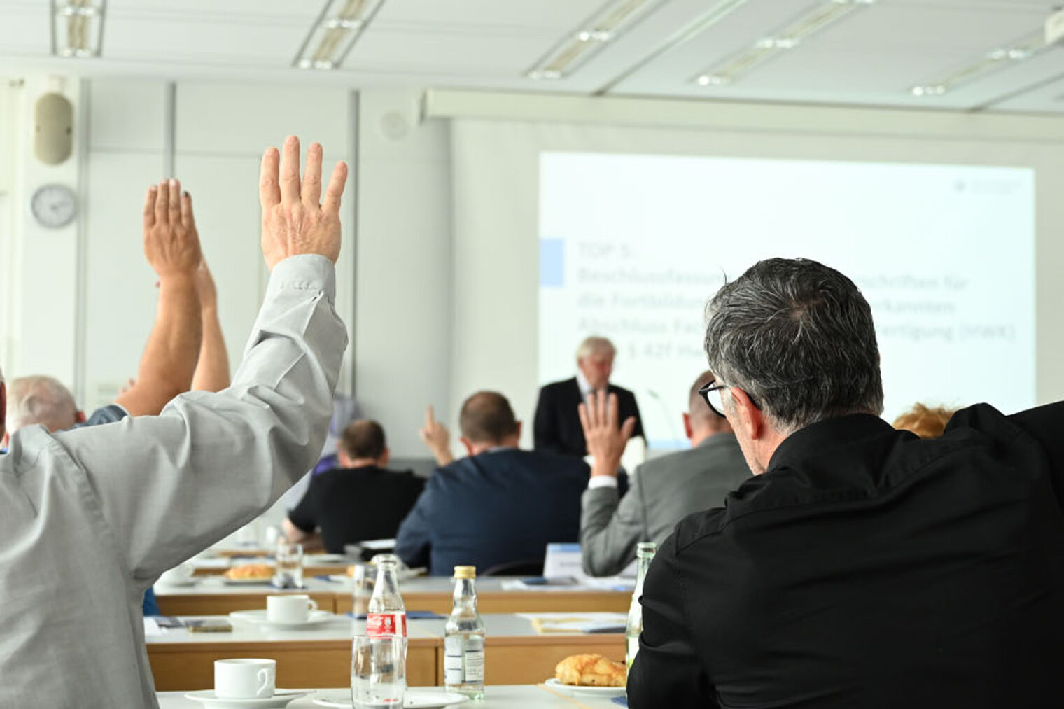 Foto von Mitgliedern der Vollversammlung, die die Hand zum Abstimmen heben