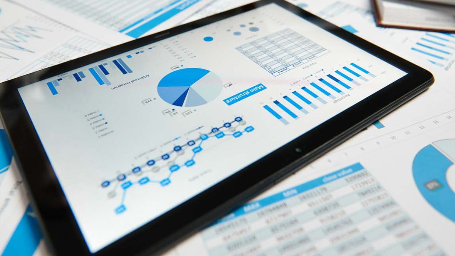 Tablet und Zettel mit Diagrammen und Zahlen auf einem Schreibtisch