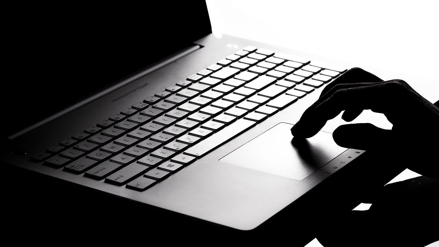 Dunkles Foto mit schwarzem Laptop und Hand im Schatten als Symbolbild für Cyber Crime