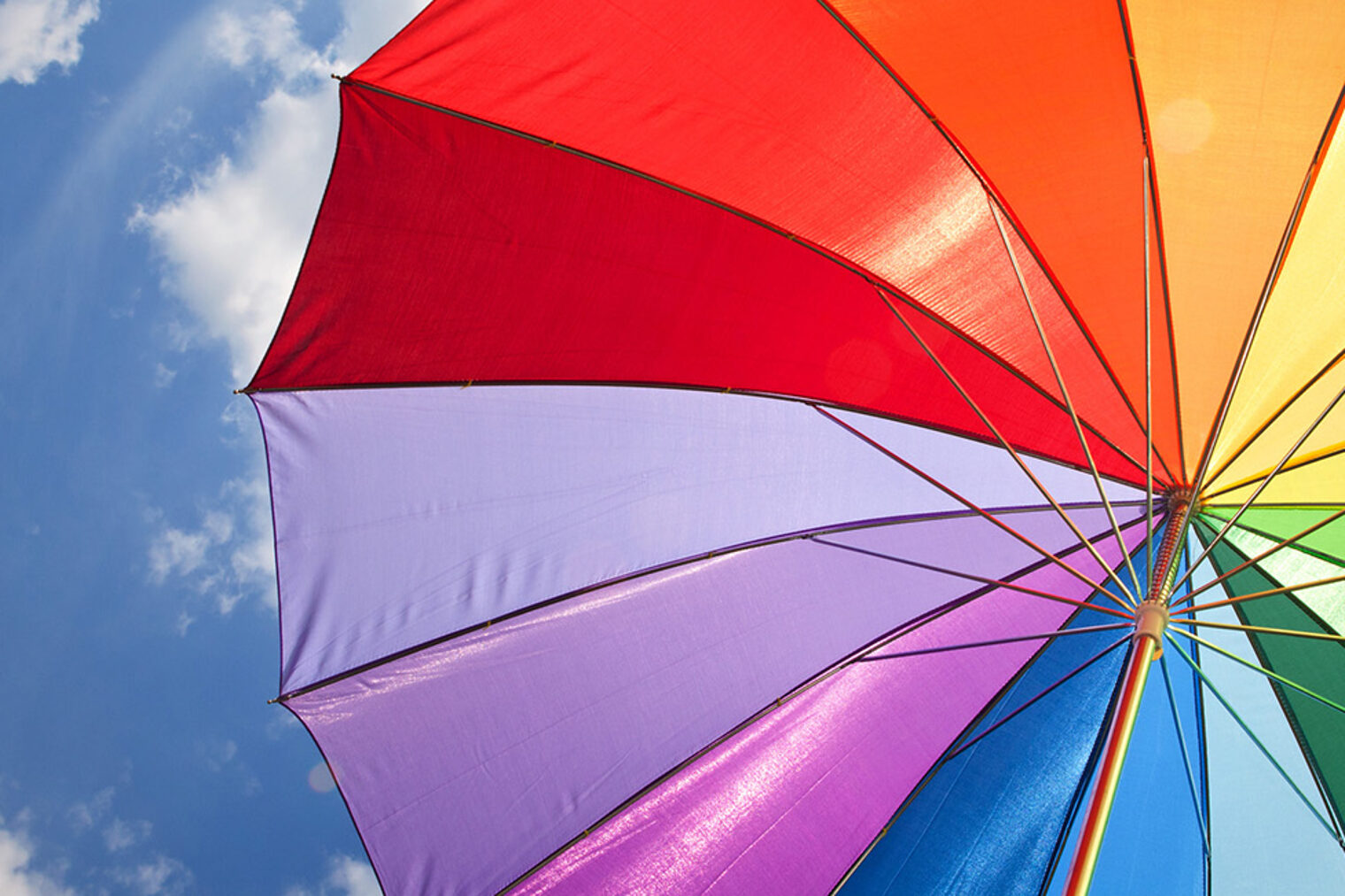 Bunter Sonnenschirm in Regenbogenfarben vor blauem Himmel mit Wolken
