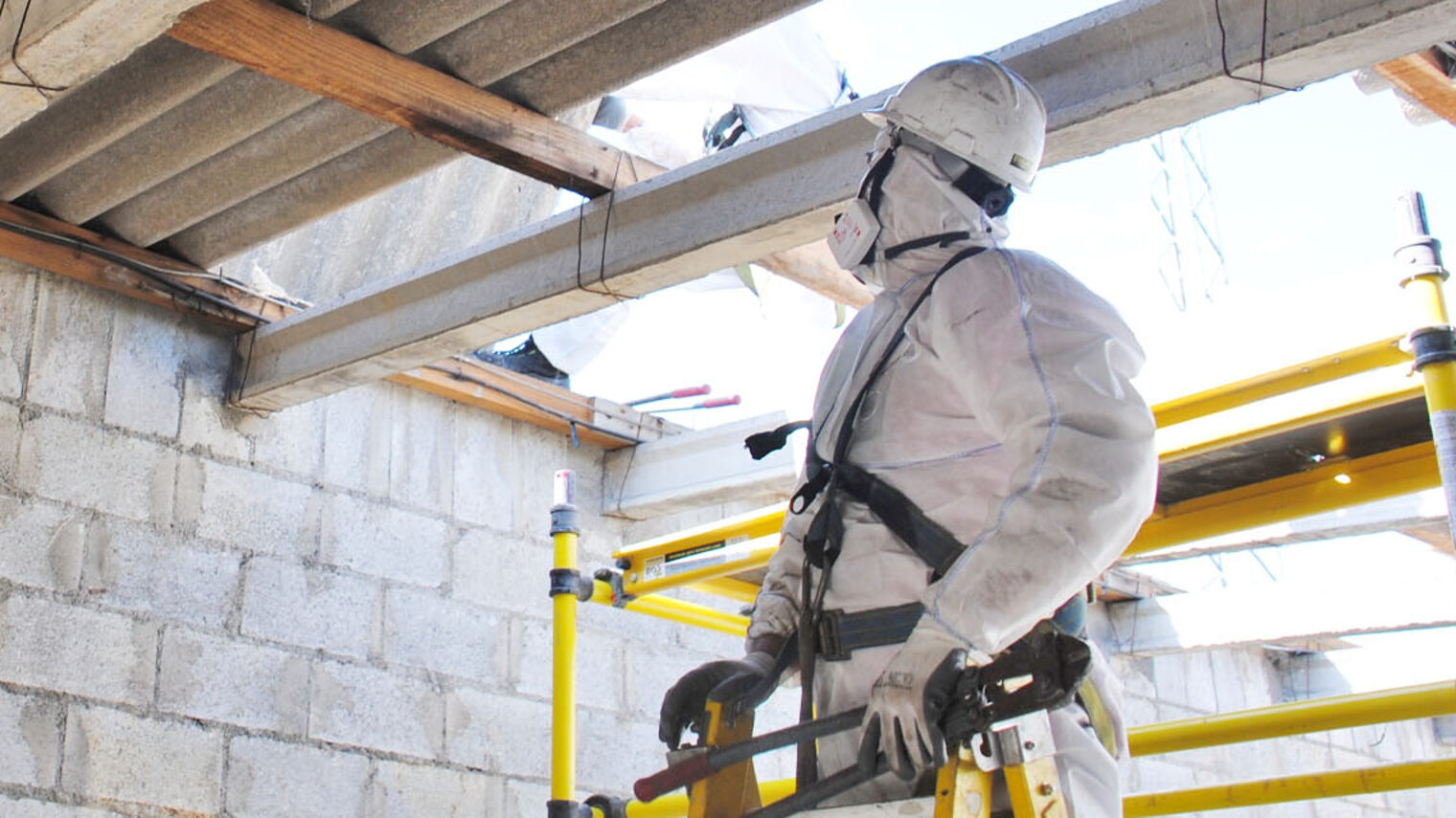Bauarbeiter in Schutzanzug auf Baustelle vor Asbestplatten