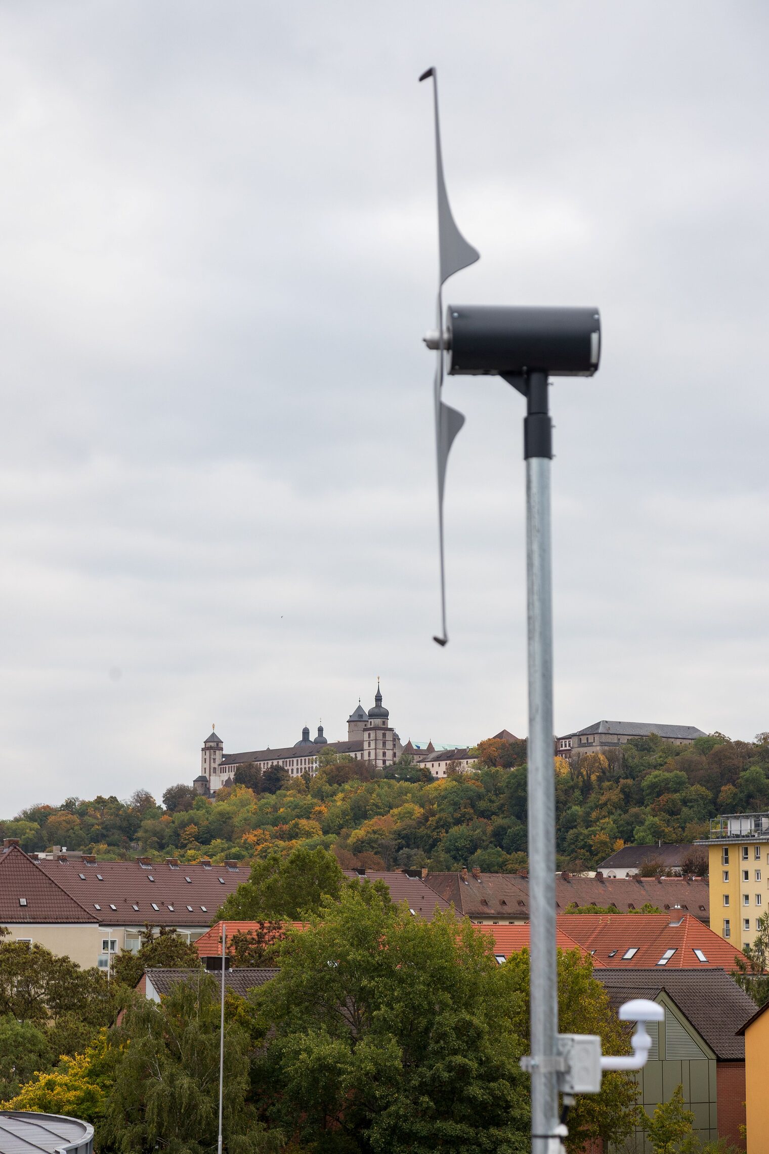 Man sieht ein kleines Windrad auf einem Dach mit der Würzburger Festung im Hintergrund