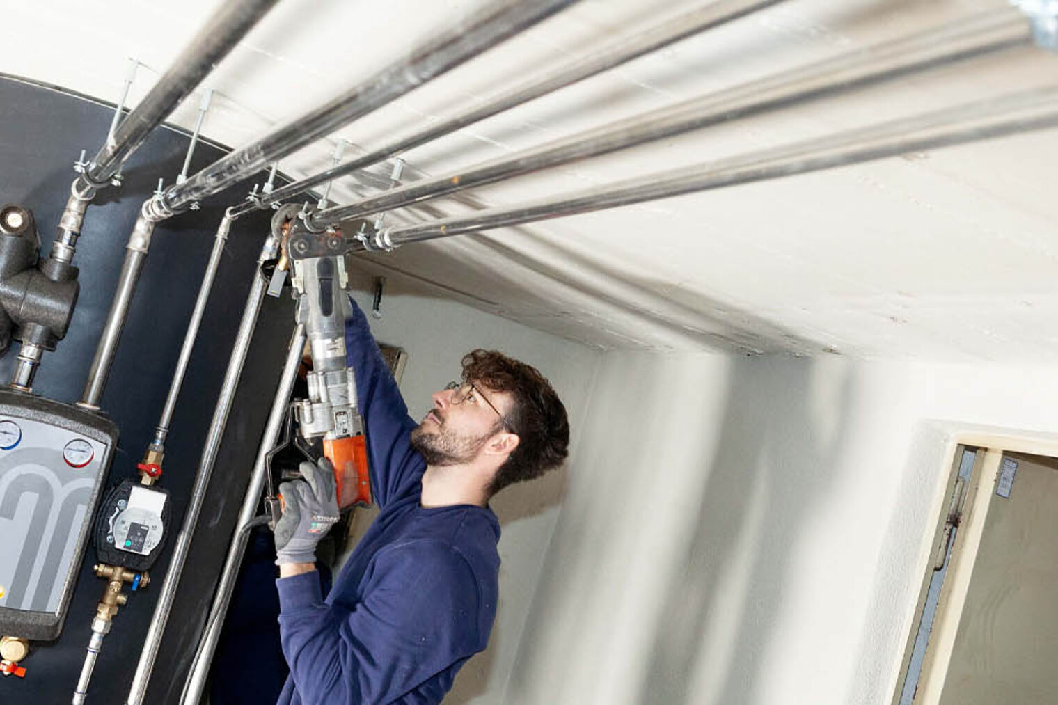 Anlagenmechaniker schraubt an Rohren eines Kessels