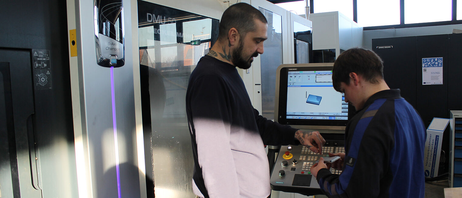 Schüler eines CNC-Intensivkurses an der Drehmaschine im Gespräch mit Feinwerktechnik Ausbilder im Bildungszentrum Aschaffenburg